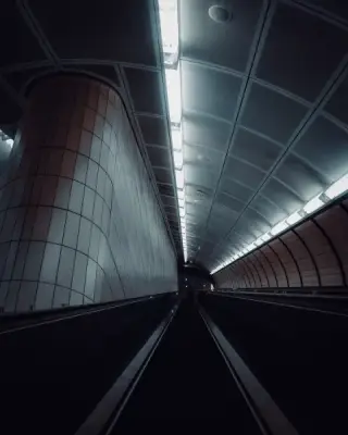 Empty curved subway escalator descending beneath fluorescent lights