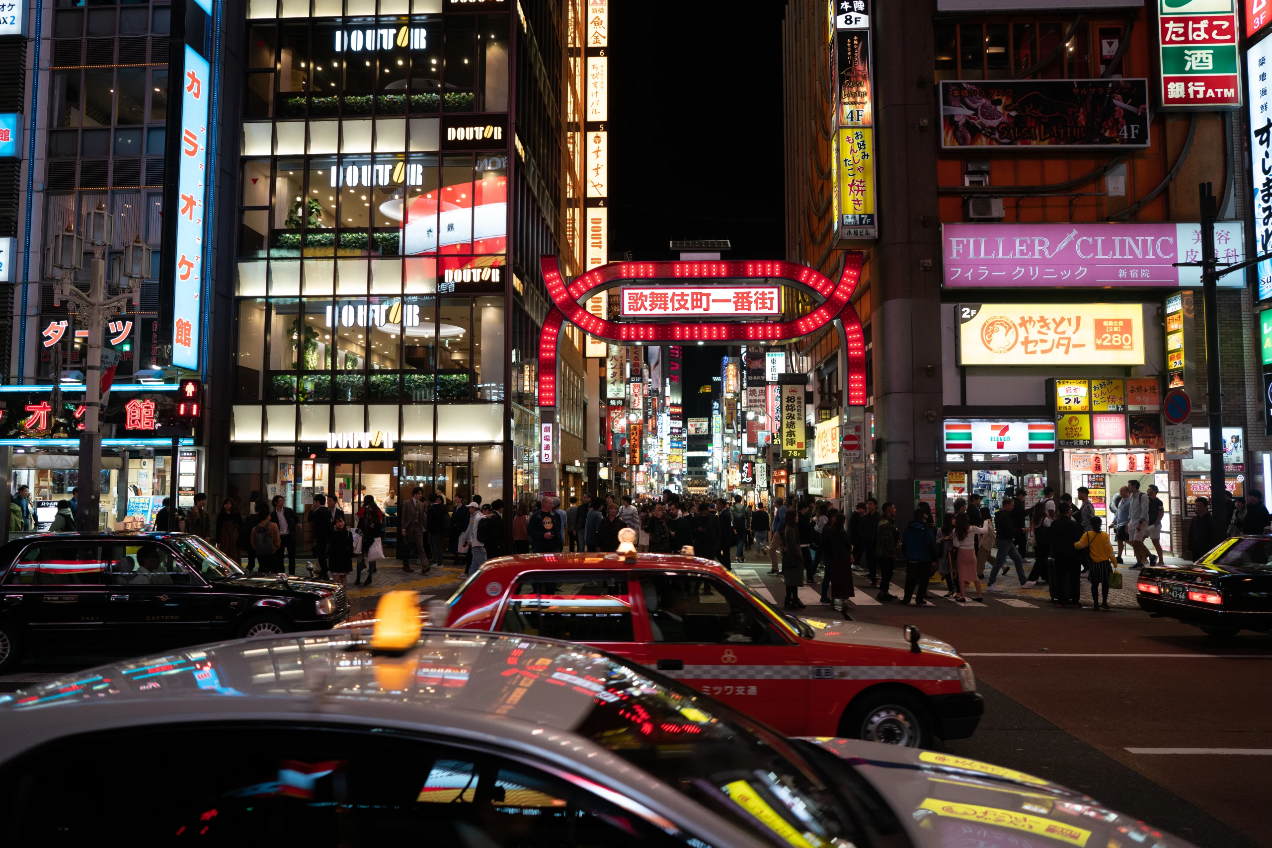 Taxis cross a neon-lit intersection at night.
