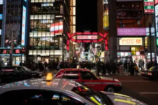 Taxis cross a neon-lit intersection at night.