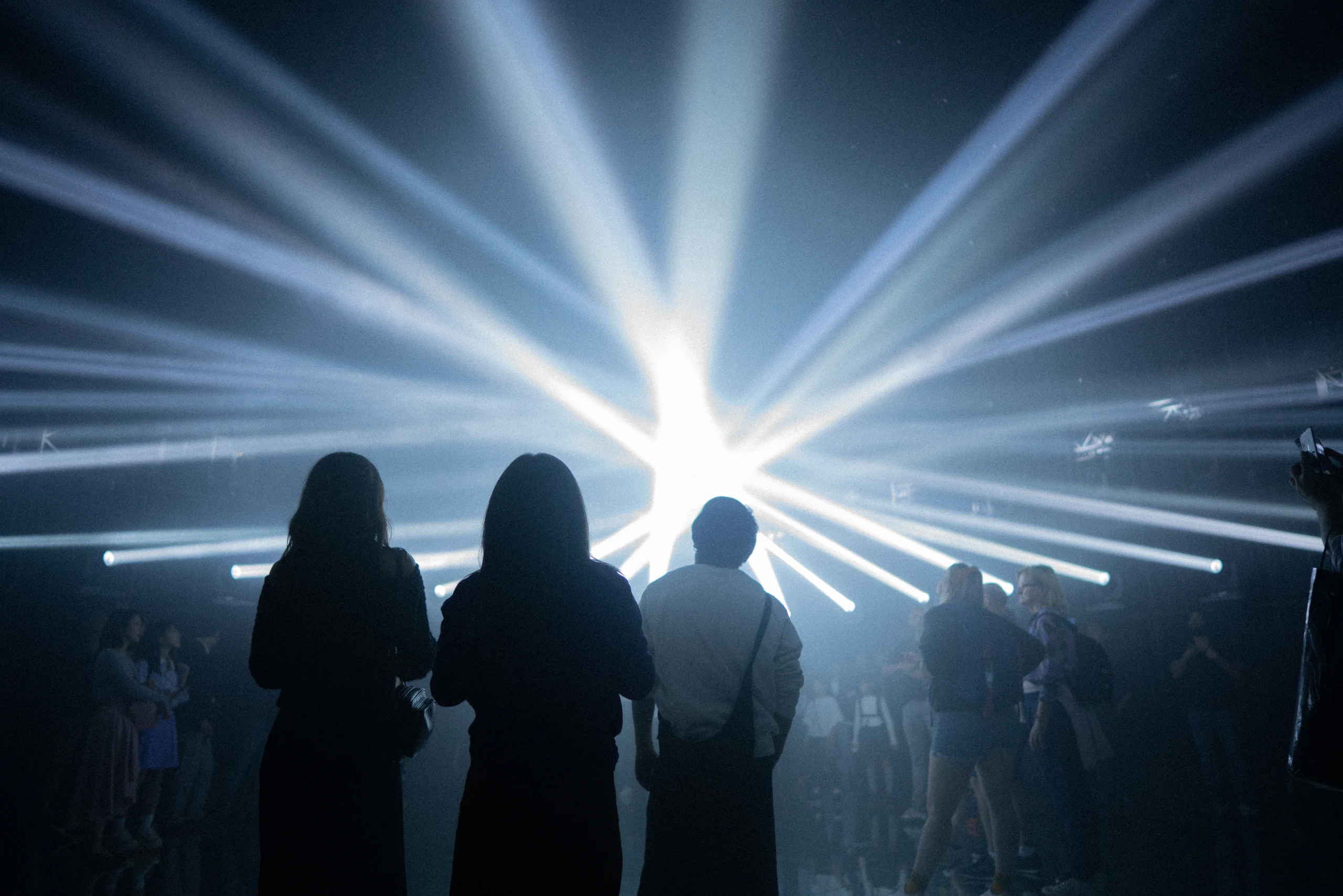Four visitors stand in silhouette before bright white beams.