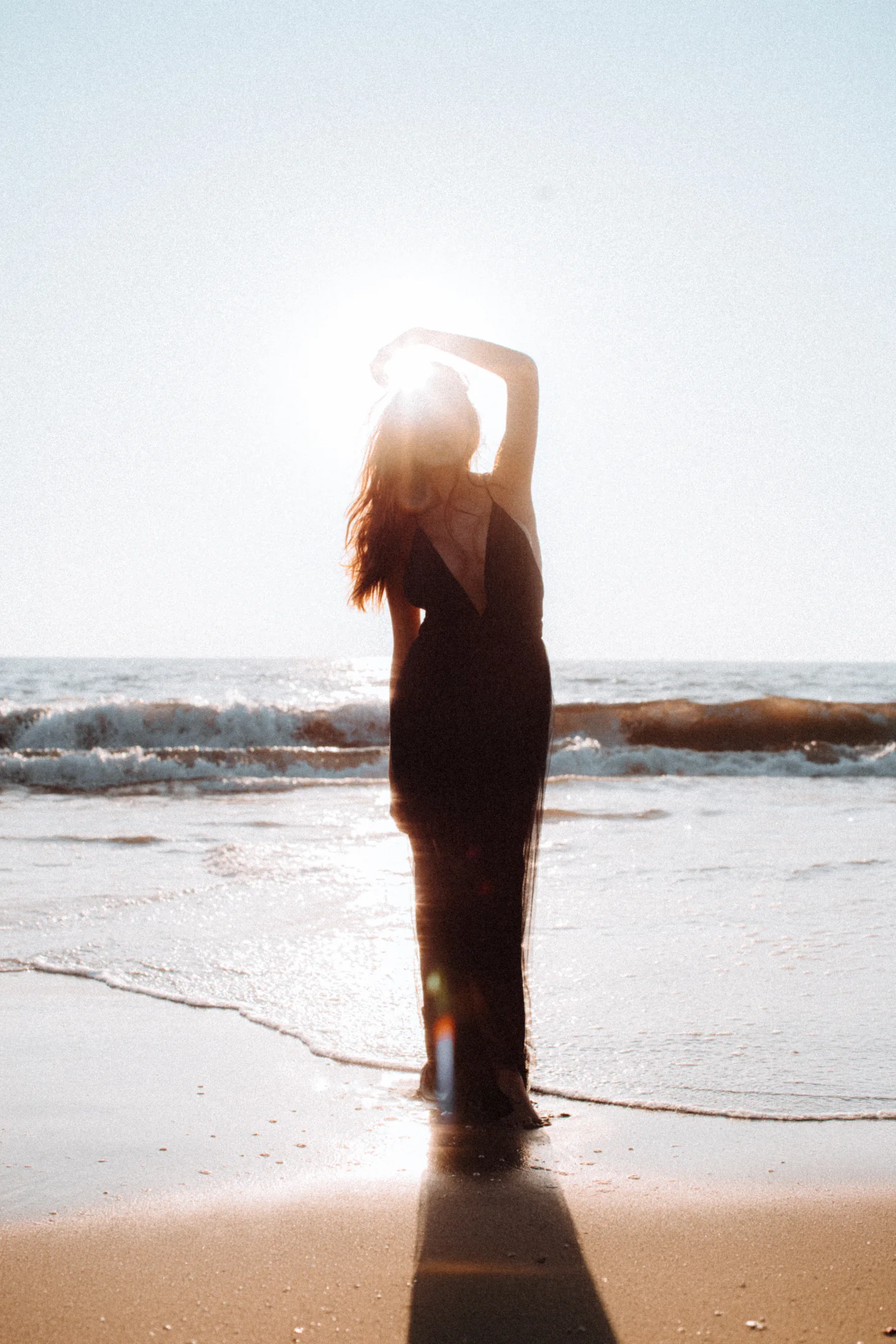 Backlit woman lifting her arms in the surf.