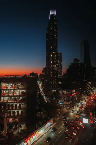 A nighttime Manhattan avenue viewed from above with traffic and a tall dark tower.