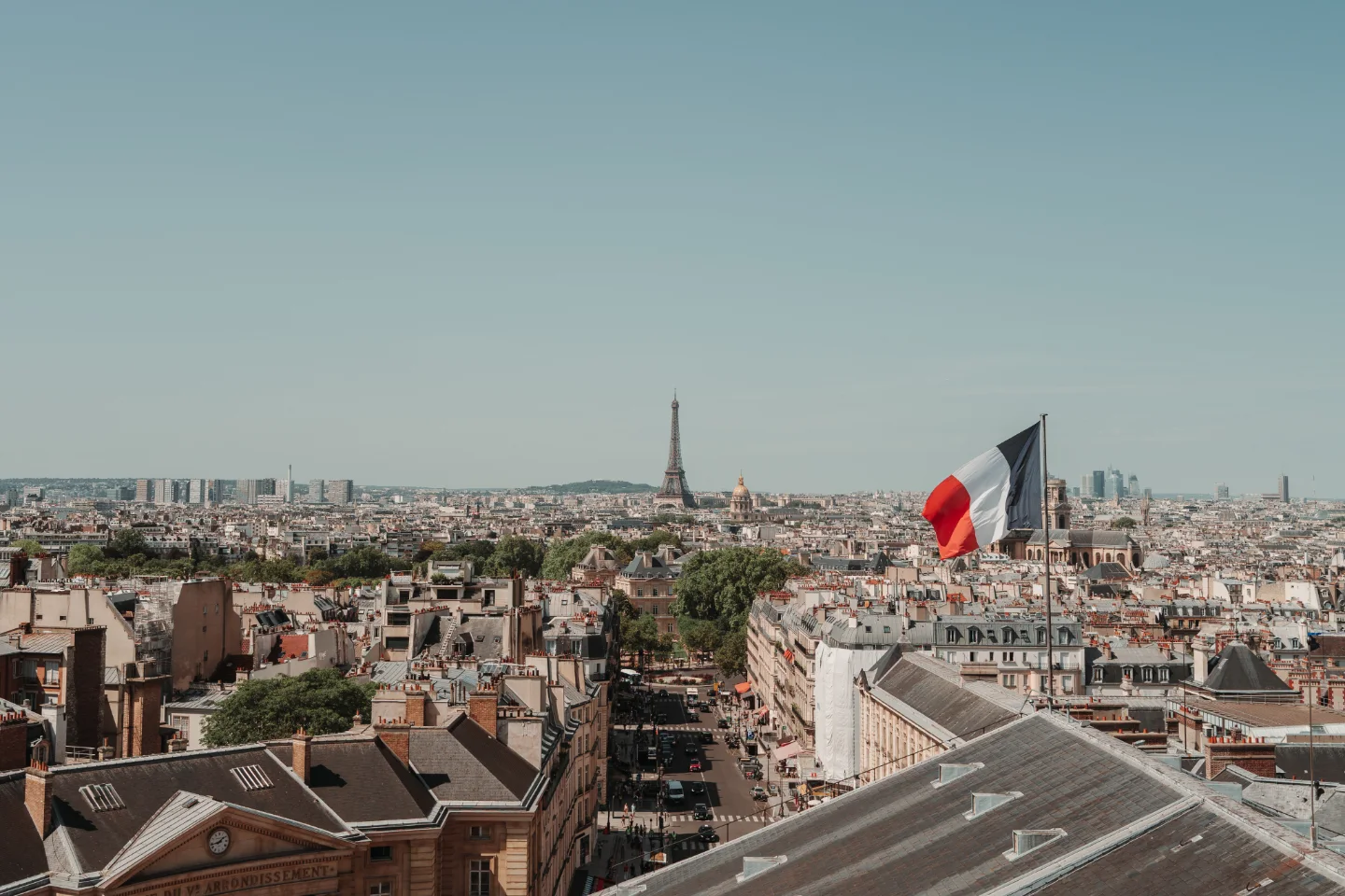 View across Paris rooftops toward the Eiffel Tower, with a large French flag in the foreground.