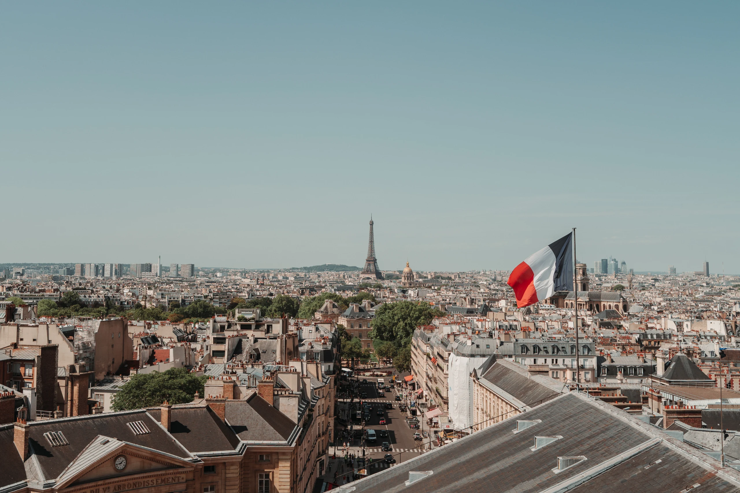 View across Paris rooftops toward the Eiffel Tower, with a large French flag in the foreground.