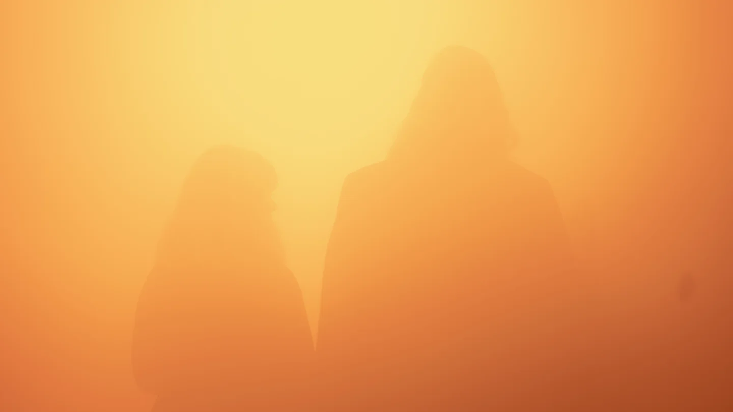 Two faint human silhouettes behind a glowing orange translucent surface.