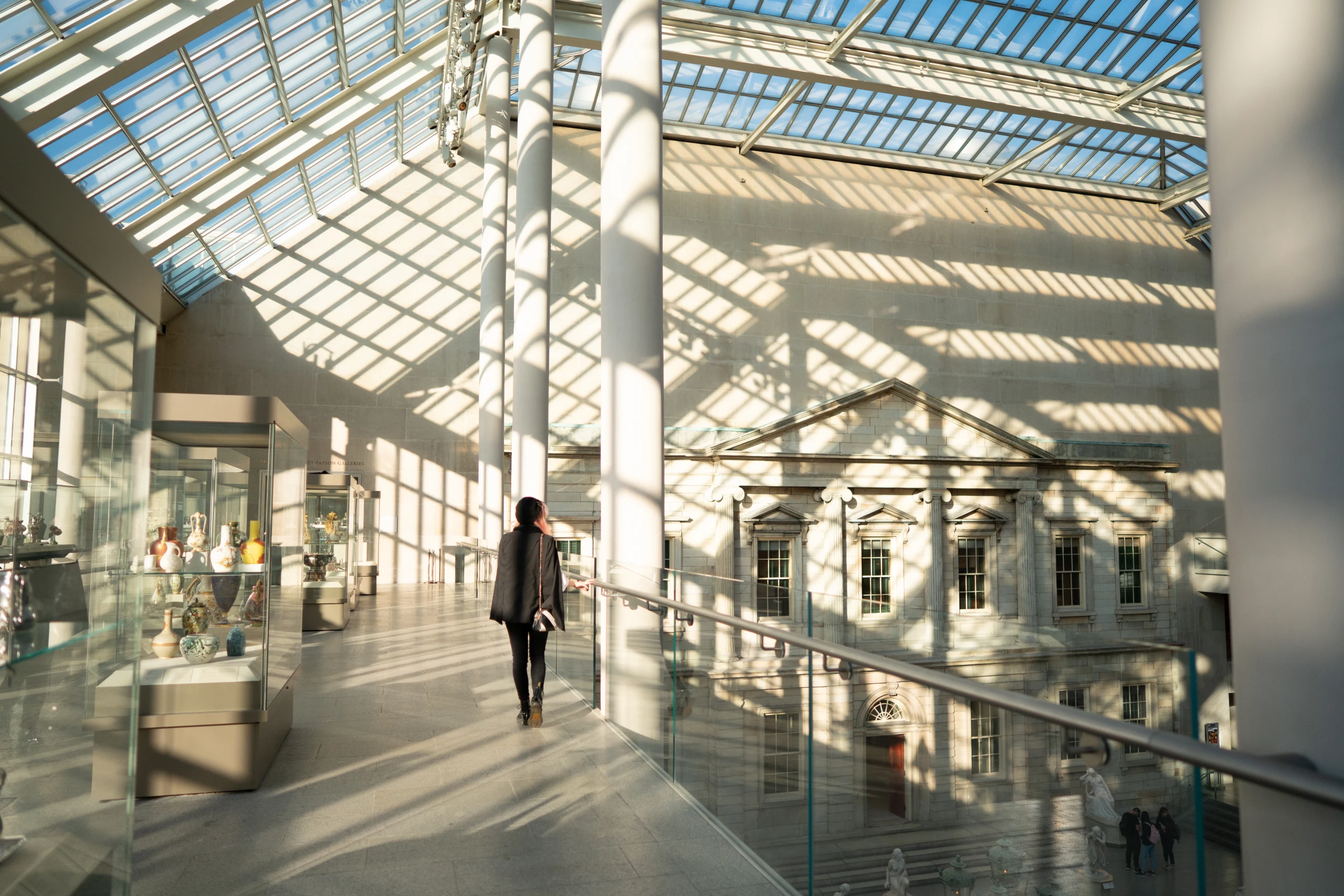 A person walking through a sunlit museum corridor under a glass atrium.