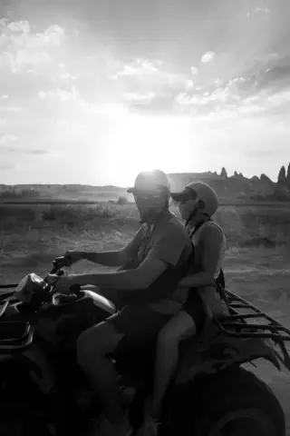 Two riders backlit on an all-terrain vehicle in black and white.