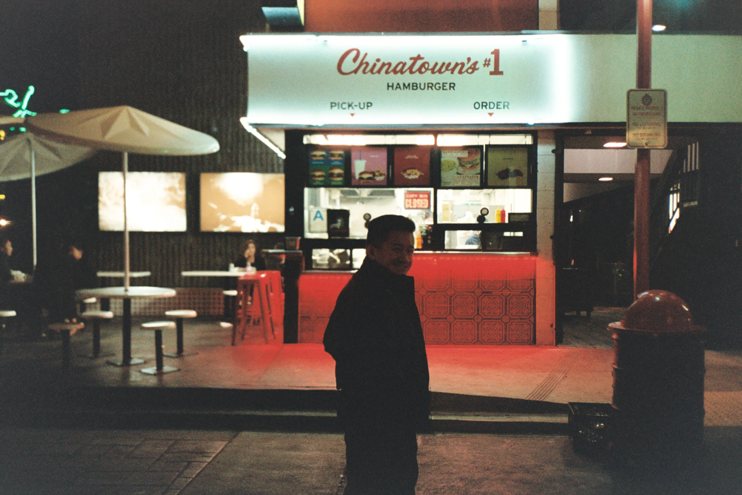 Man silhouetted outside a red Chinatown burger counter.
