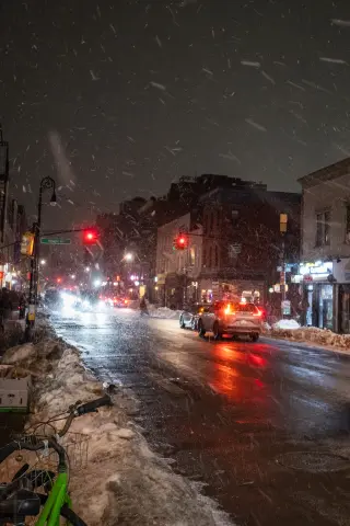 A wet snowy city street at night with cars and red traffic lights.