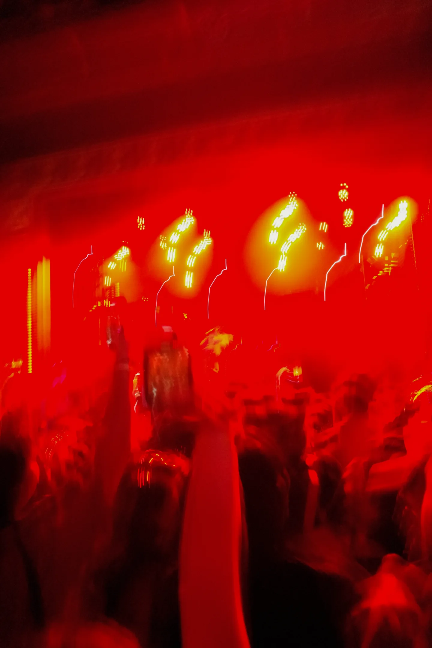 Blurred crowd with raised hands beneath intense red and yellow stage lights.