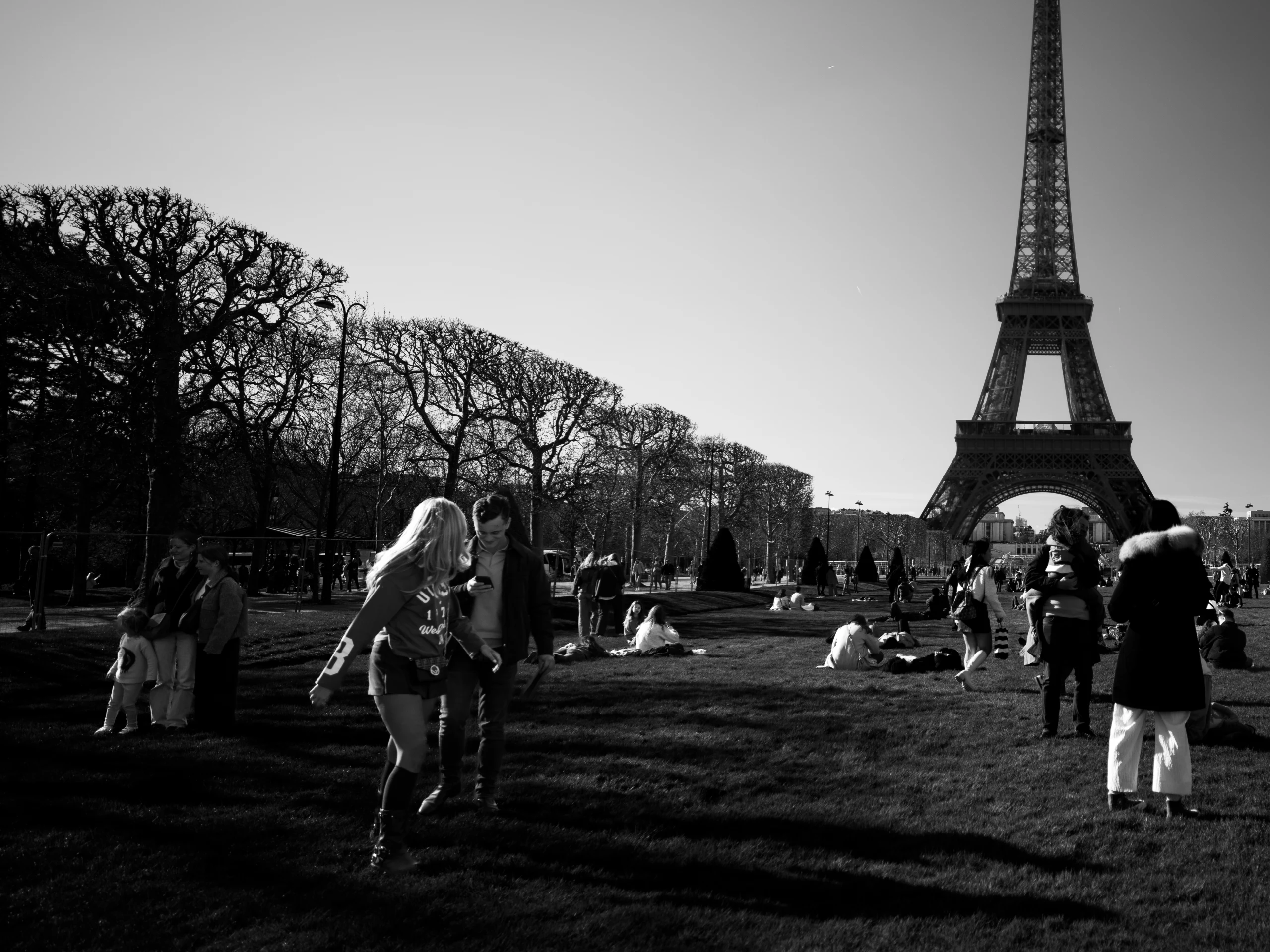 Monochrome view of people gathered on a lawn beneath the Eiffel Tower.