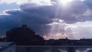 Sunbeams break through clouds over a low city skyline.