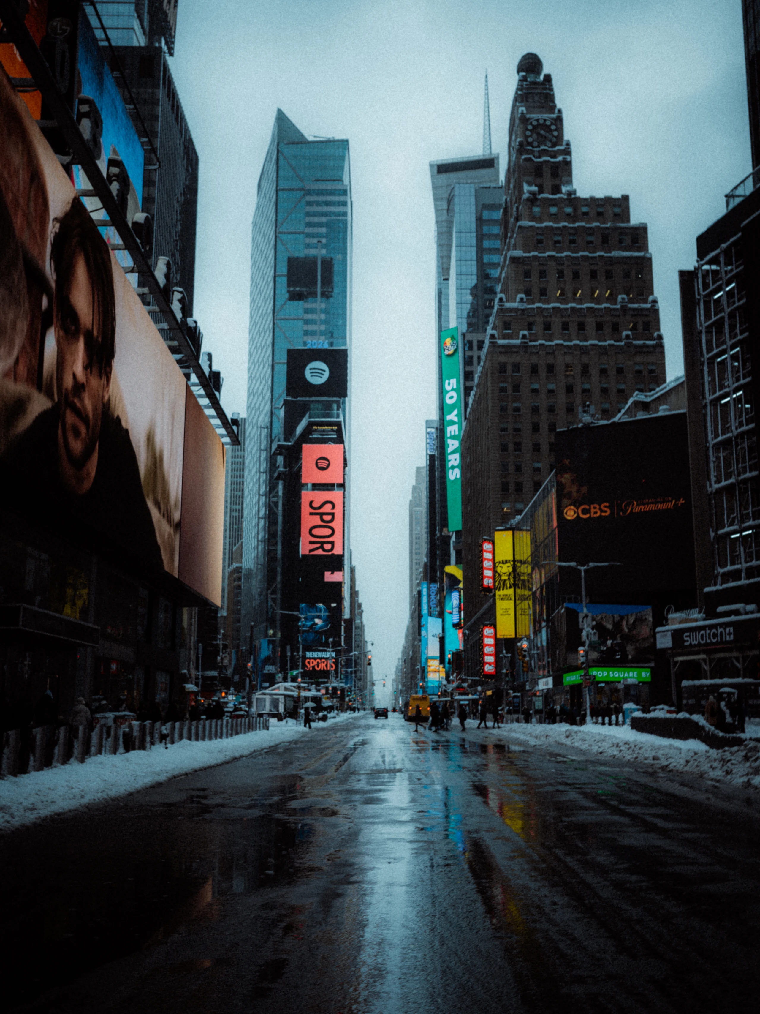 Times Square screens reflected in a wet snow-lined street