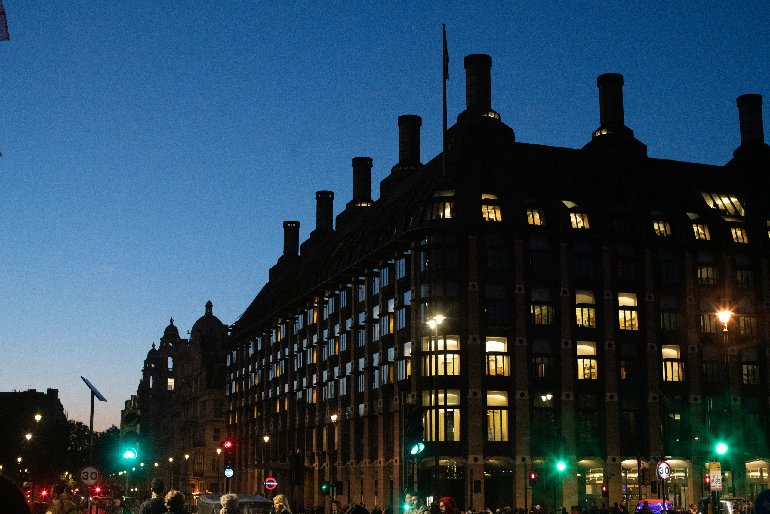 A grand curved London building glows against a deep blue evening sky.
