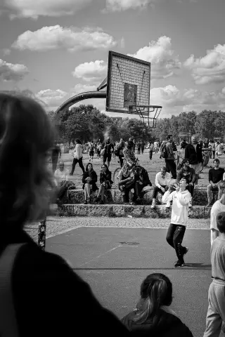 Black-and-white photograph of a basketball player beneath a weathered hoop as spectators gather at Mauerpark.