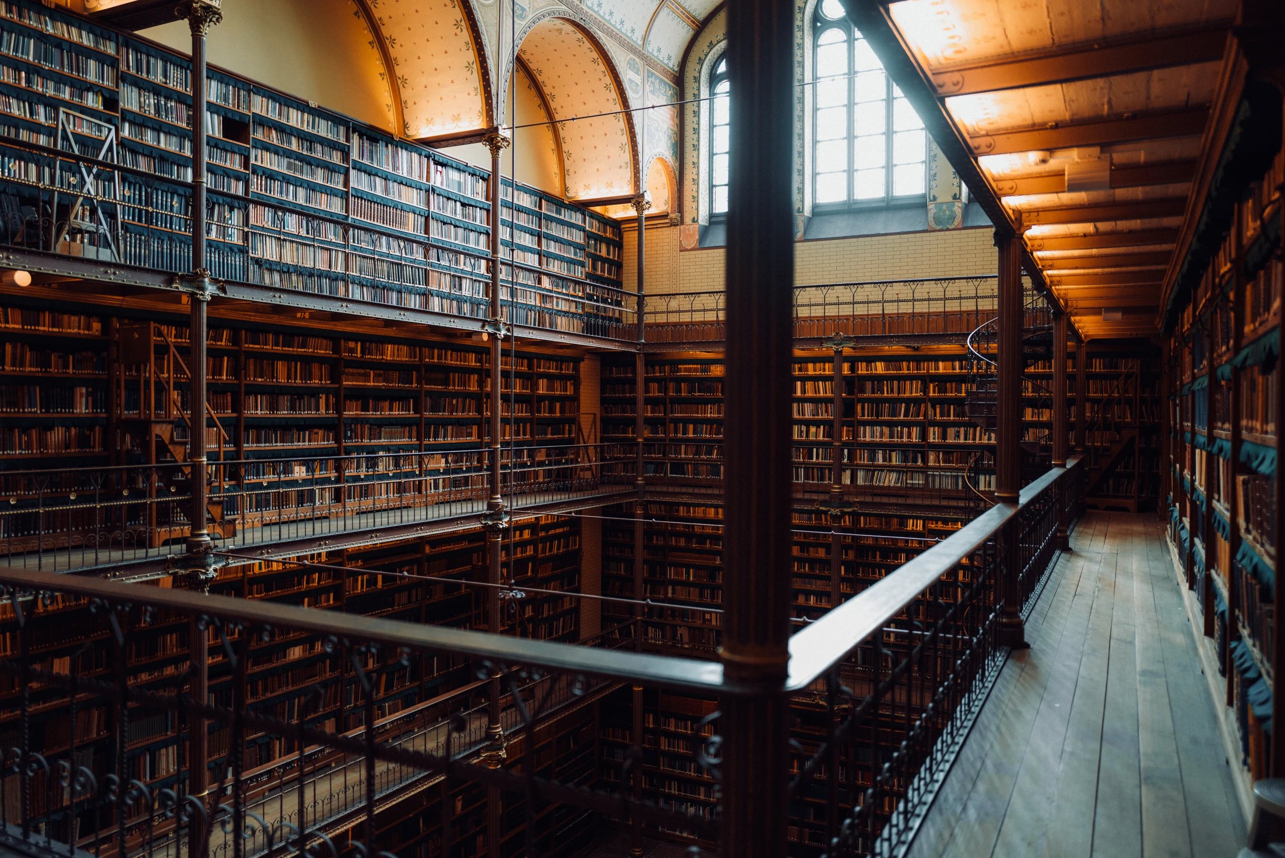 Multi-level book galleries, iron railings, arched windows, and warm reading lights inside the Cuypers Library.