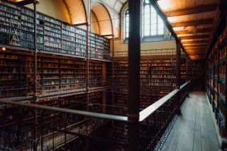 Multi-level book galleries, iron railings, arched windows, and warm reading lights inside the Cuypers Library.