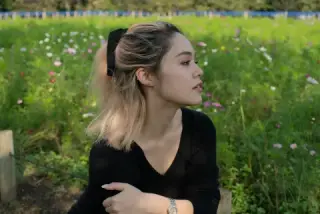 A profile portrait of a woman against green grass and flowers.