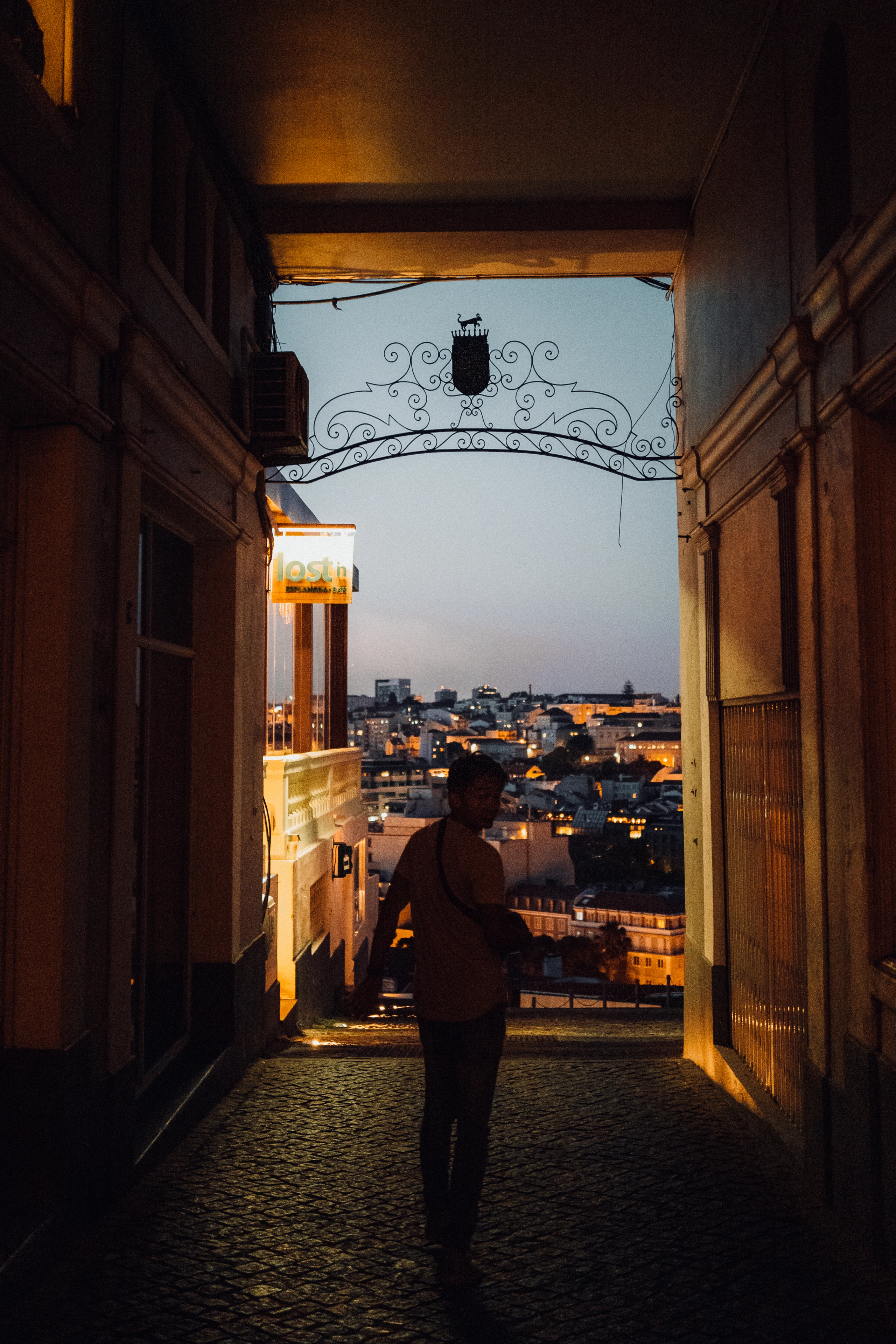 A lone figure stands in a doorway overlooking Lisbon at dusk.