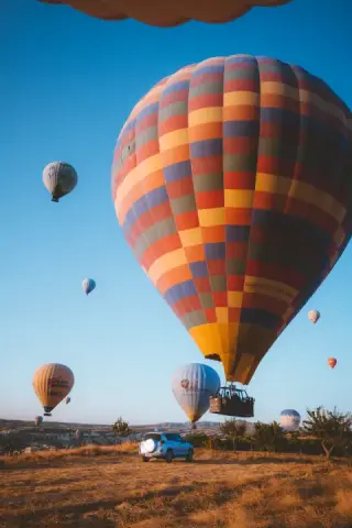 Large striped hot-air balloon rising close above the field.