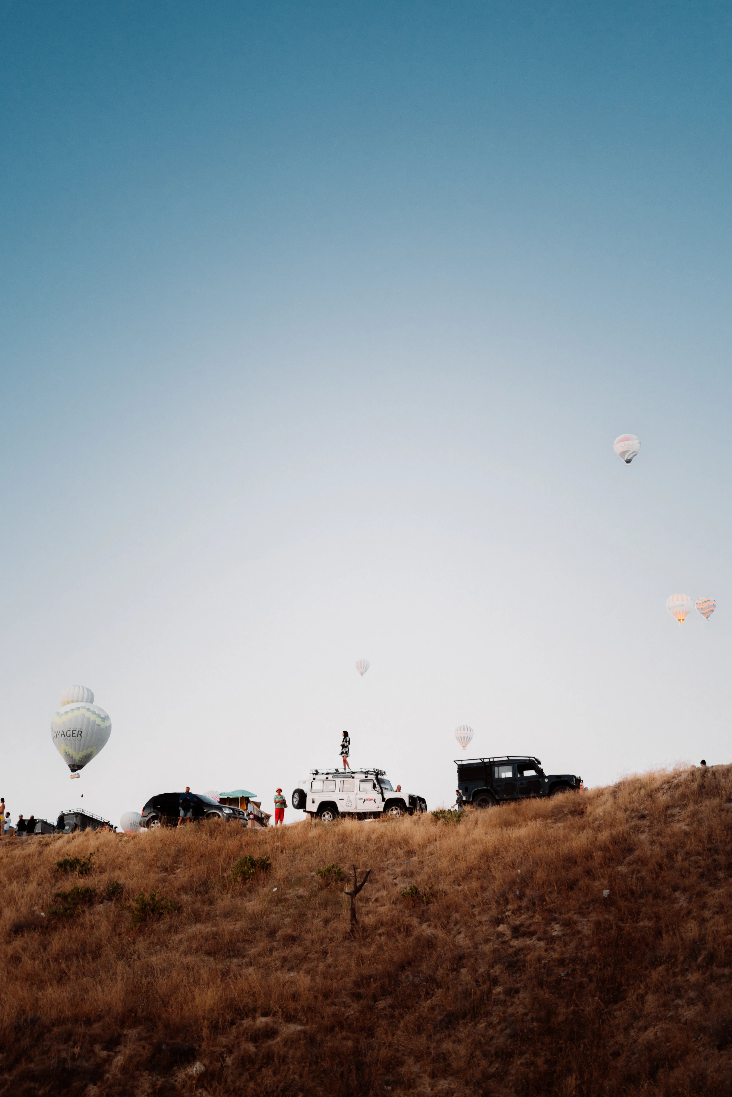 Three distant hot-air balloons above scrubland.