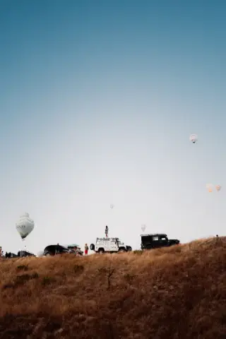 Three distant hot-air balloons above scrubland.