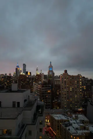 The Manhattan skyline at blue hour under heavy gray clouds, with the Empire State Building lit blue and gold above dense rooftops.