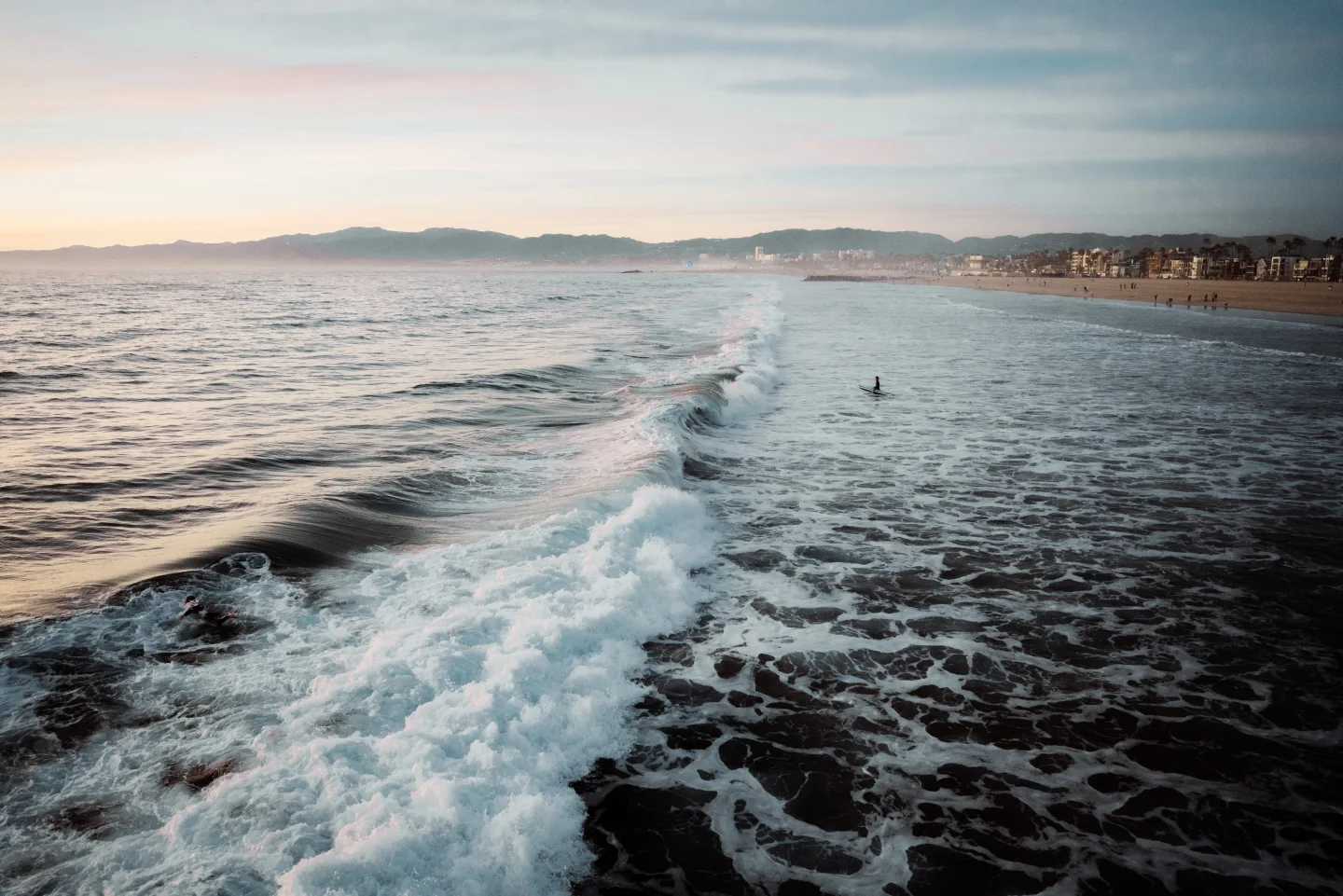 Wave breaking along a broad shoreline with swimmers in the distance.