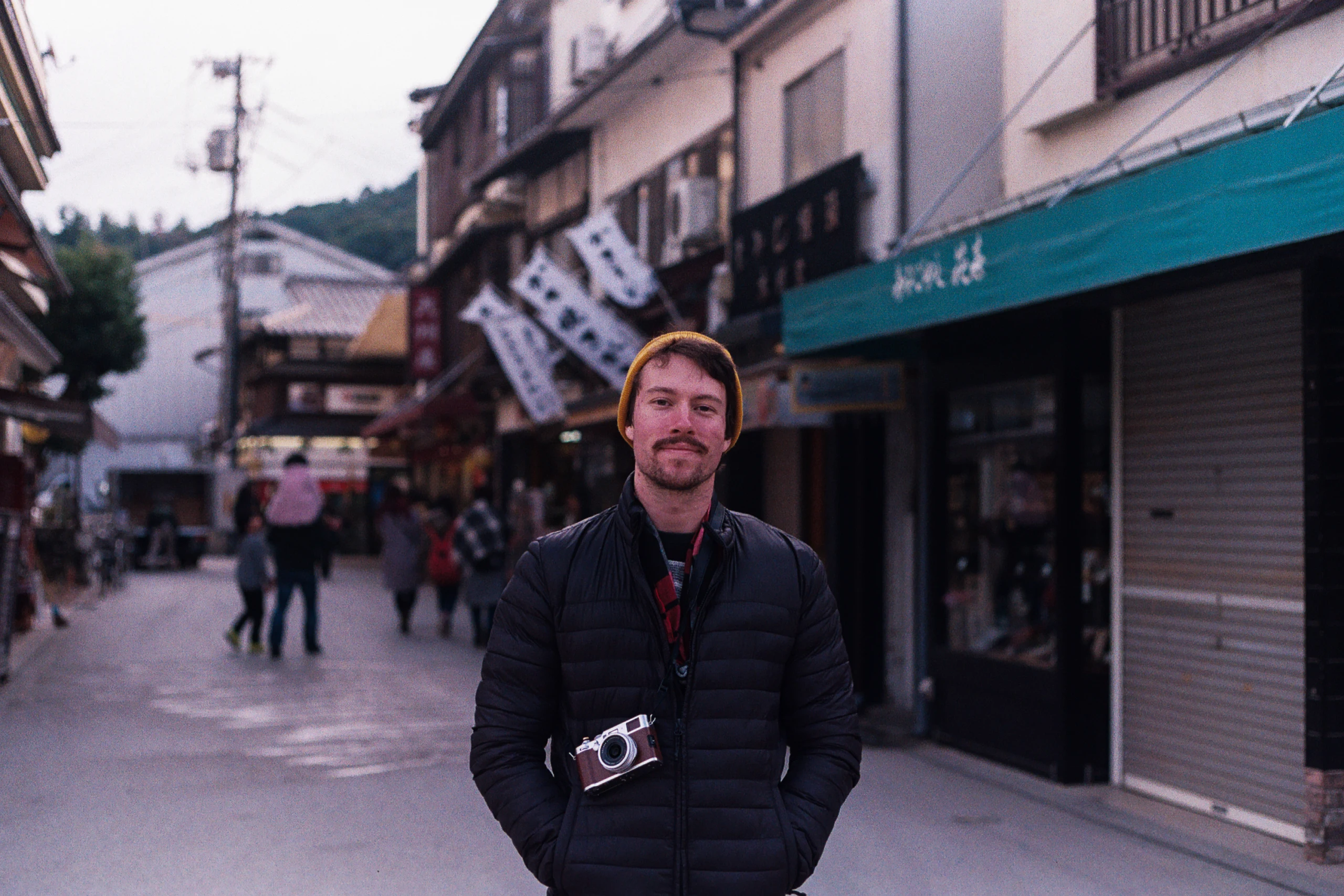 A man with a film camera stands on a pedestrian street in Miyajima.