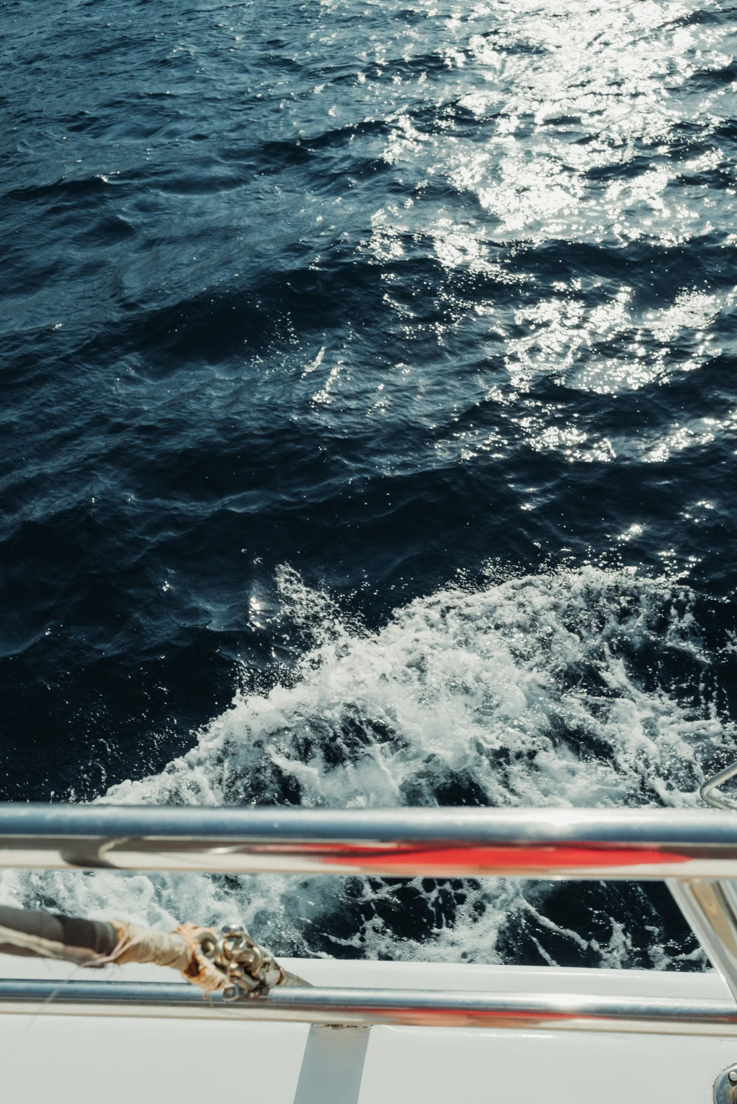 Dark Aegean water and white wake seen over a boat's metal railing.