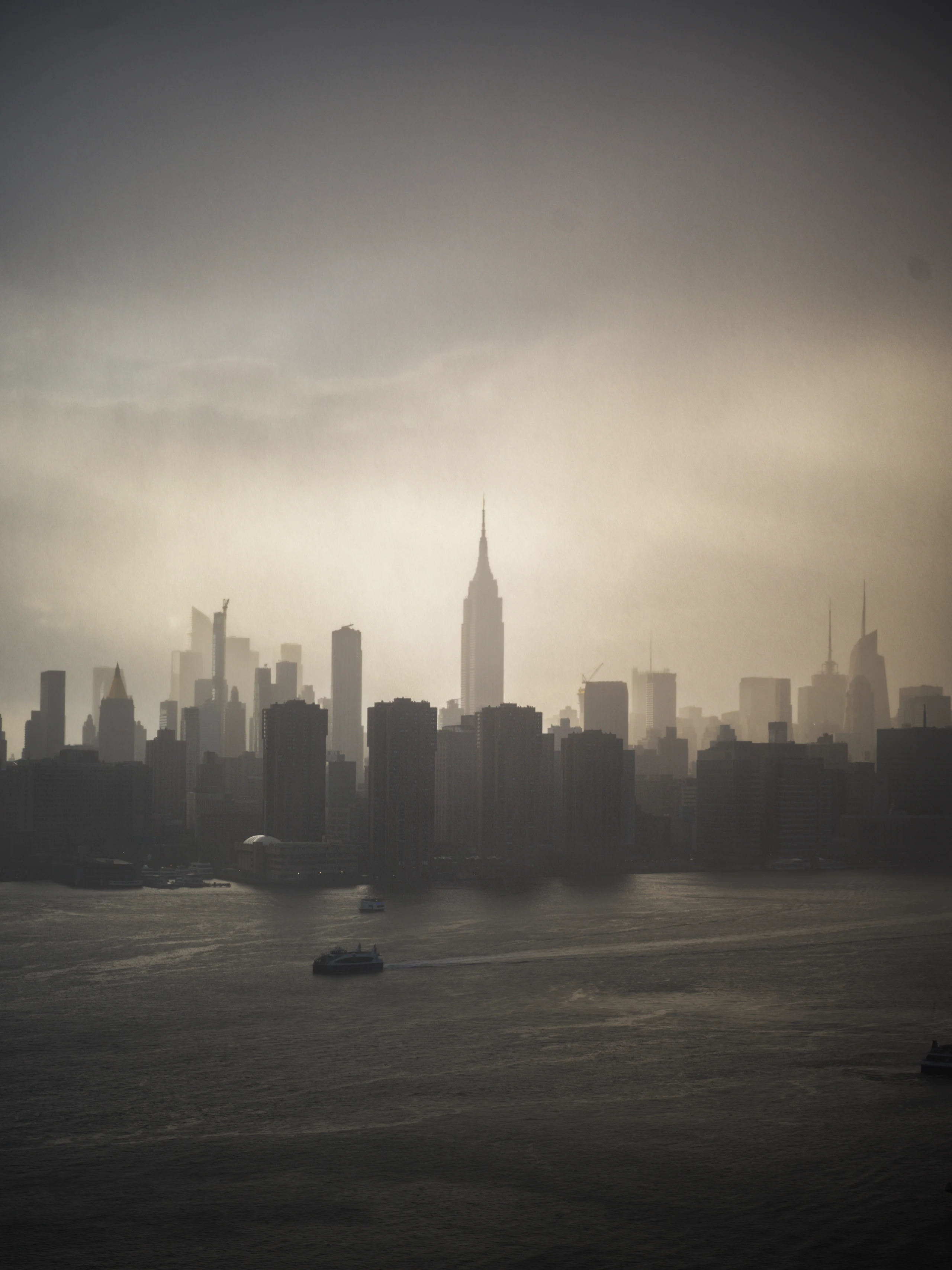 The Empire State Building and Manhattan skyline rise through haze across the river.