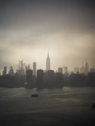 The Empire State Building and Manhattan skyline rise through haze across the river.