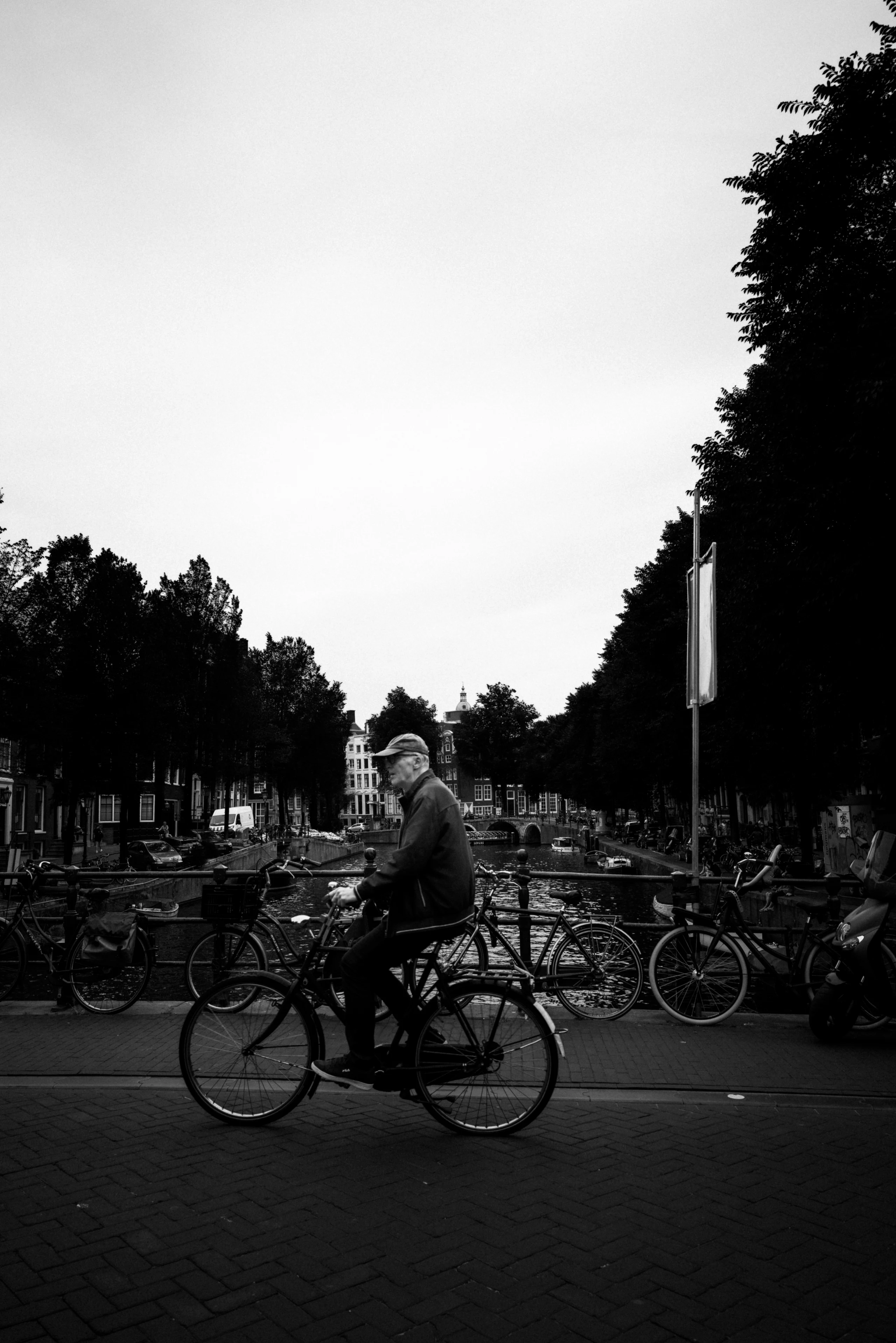 Monochrome view of a cyclist crossing a bridge lined with bicycles beside an Amsterdam canal.