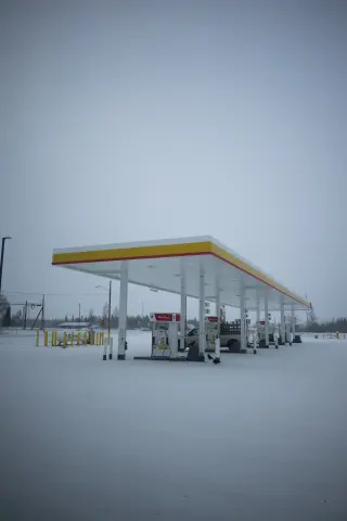 A yellow-and-red gas station canopy and fuel pumps stand in a snow-covered lot beneath a gray winter sky.
