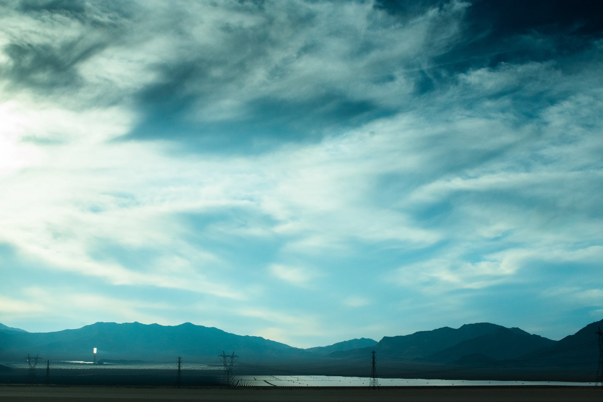 A desert highway leads toward distant mountains beneath a broad blue sky.