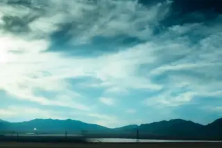 A desert highway leads toward distant mountains beneath a broad blue sky.