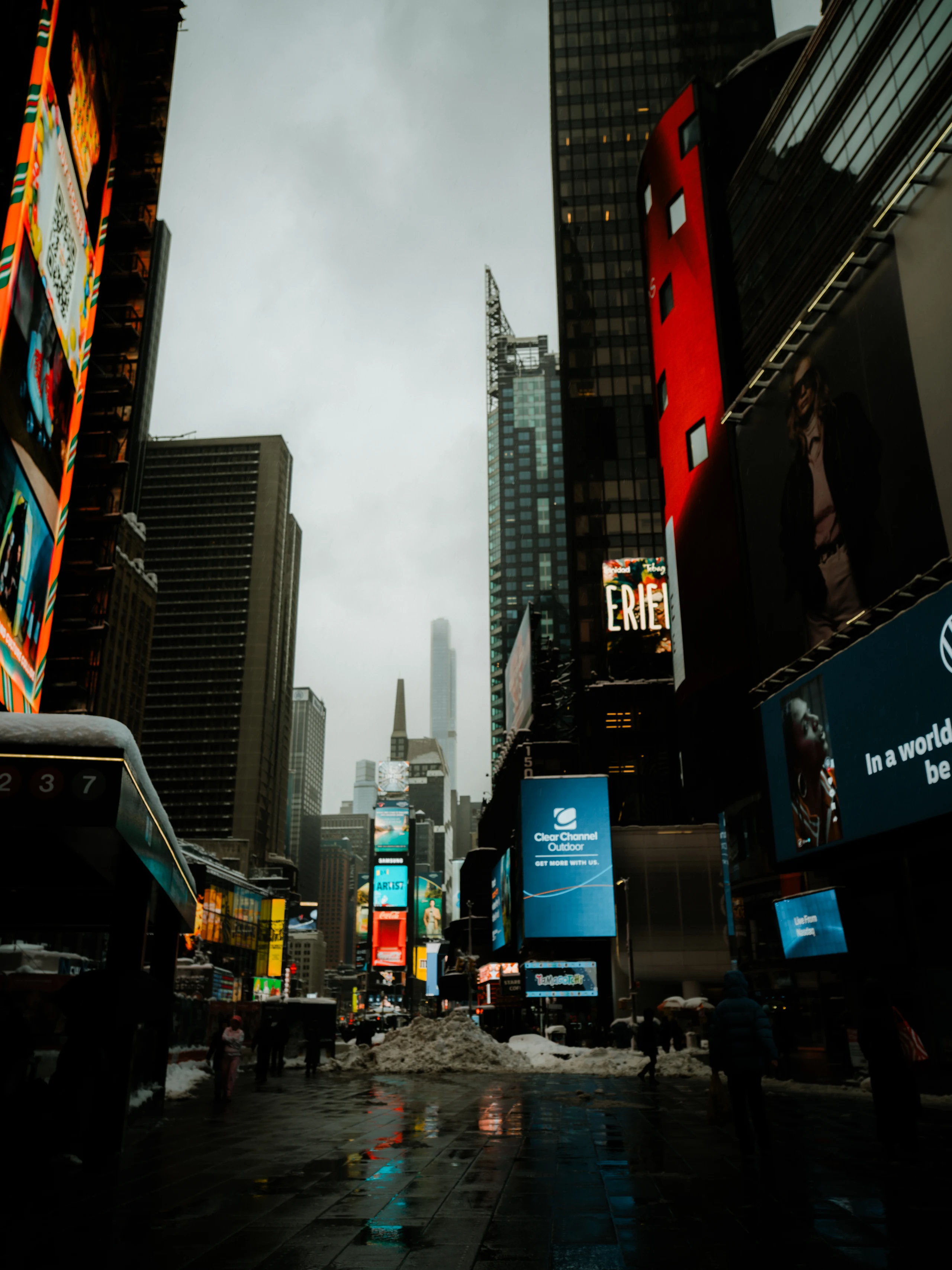 Colorful Times Square screens above wet pavement and piles of snow