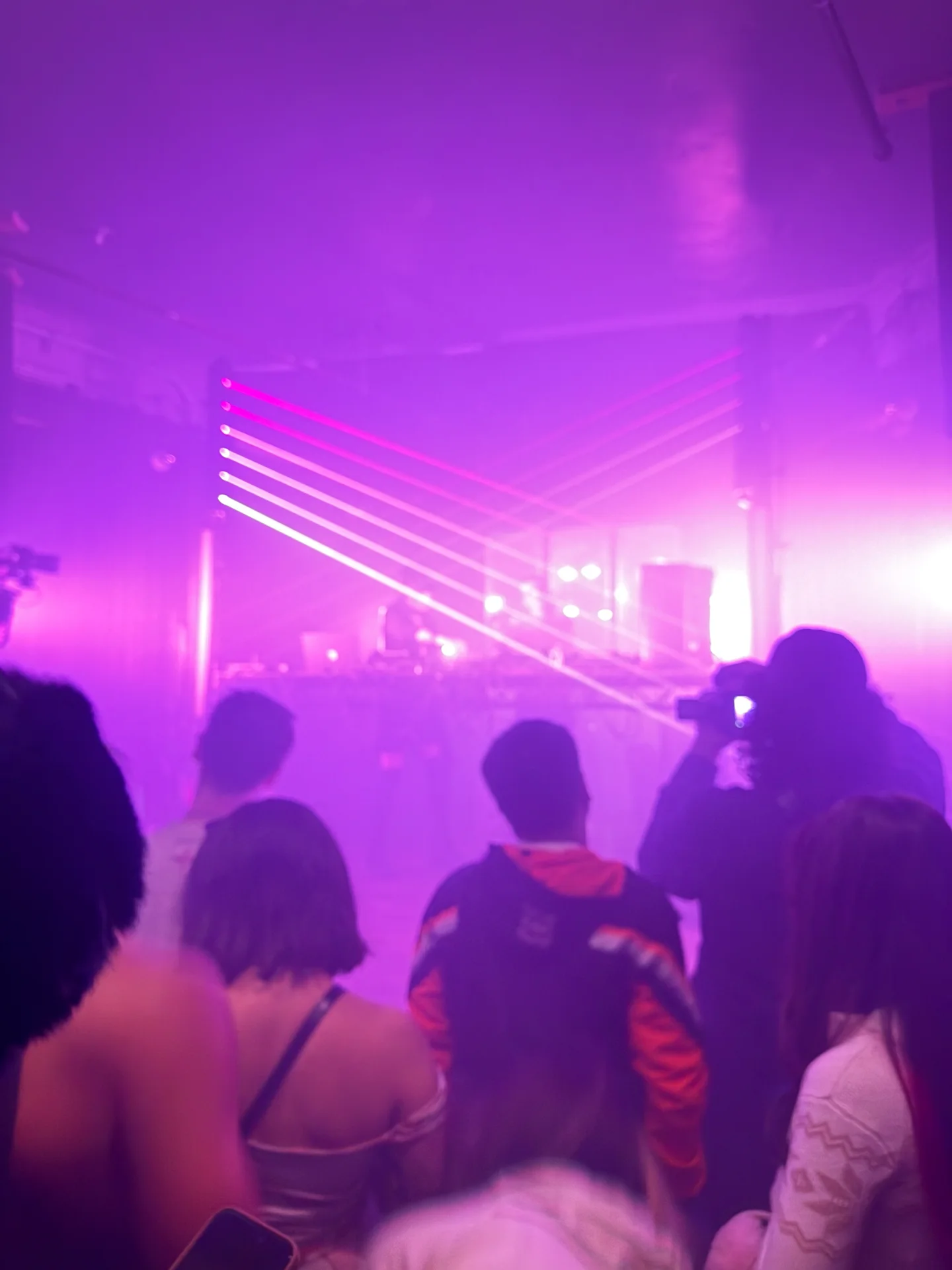 A nightclub crowd faces magenta beams cutting through haze above the dance floor.