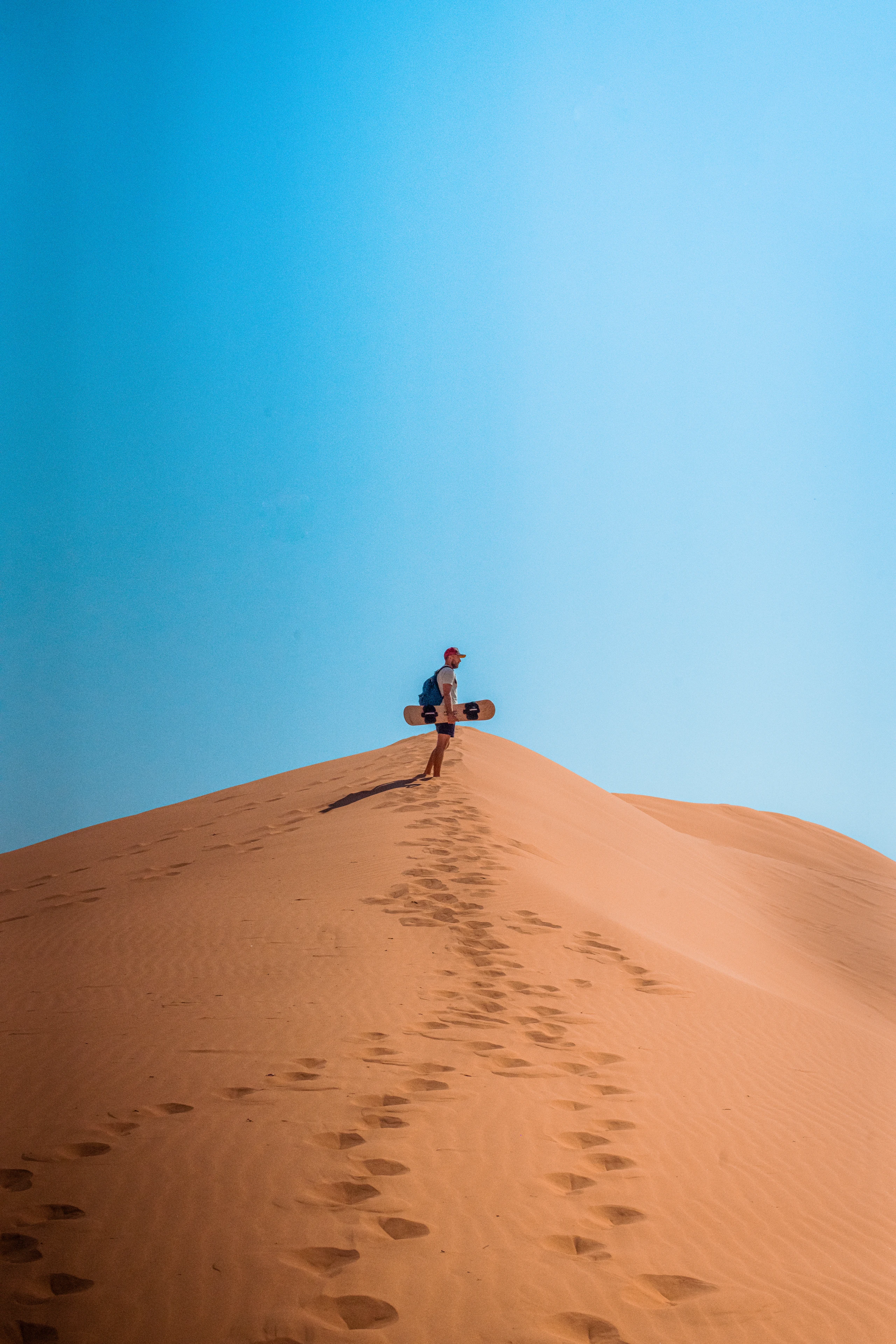 A person stands at the crest of a pale wind-shaped desert dune.
