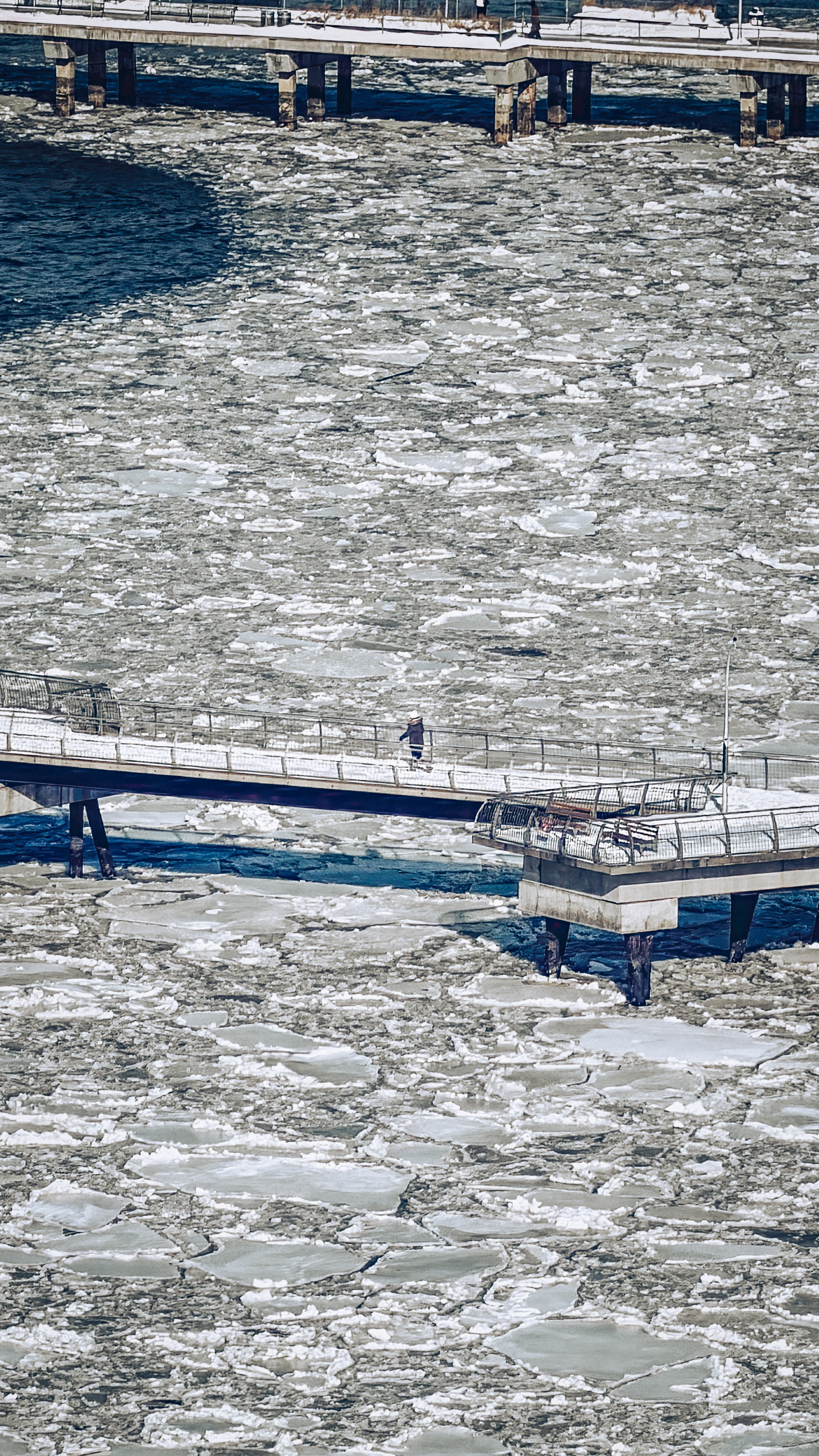 A frozen river crossed by parallel blue railings and dark channels of water.