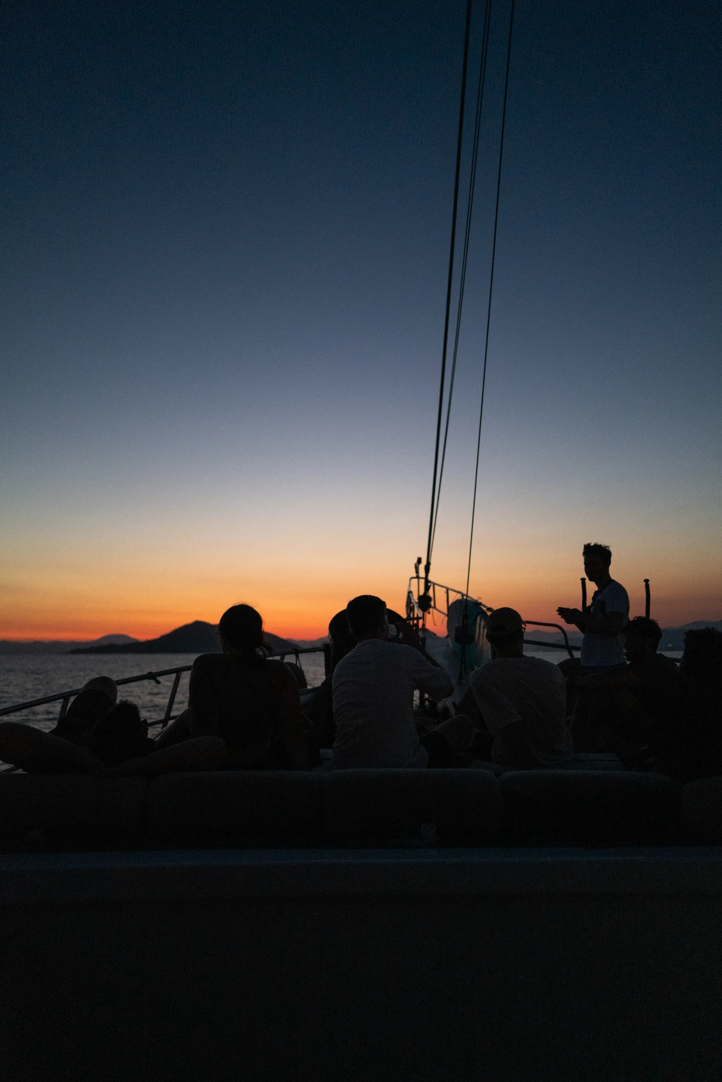 Silhouetted passengers gather on deck against an orange-blue sunset.