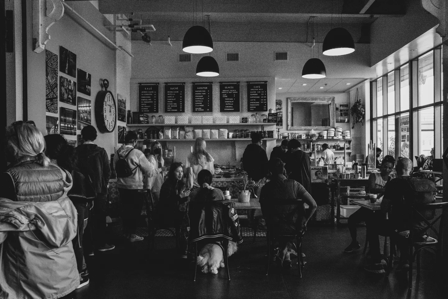 Black-and-white photograph of diners in a bright daytime cafe.