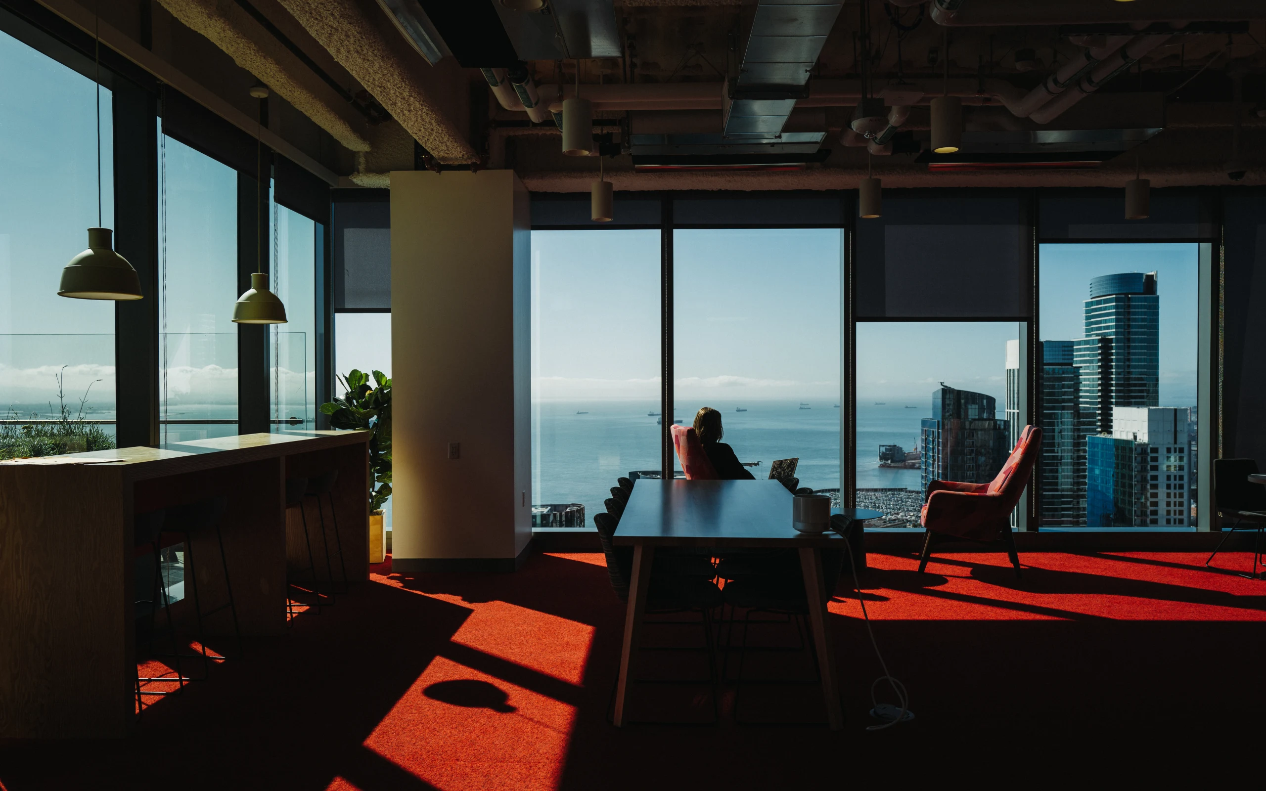 Sunlit office with red carpet and chairs overlooking the San Francisco waterfront through floor-to-ceiling windows.