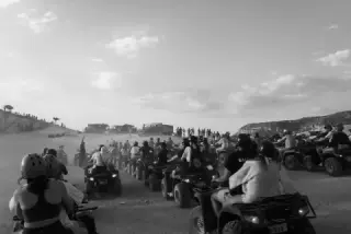 Black-and-white photograph of a crowd of ATV riders gathered on a dusty plain.