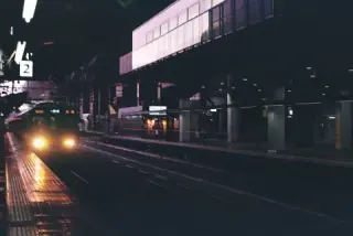 A train with bright headlights approaches a dark station platform beneath a platform 2 sign.