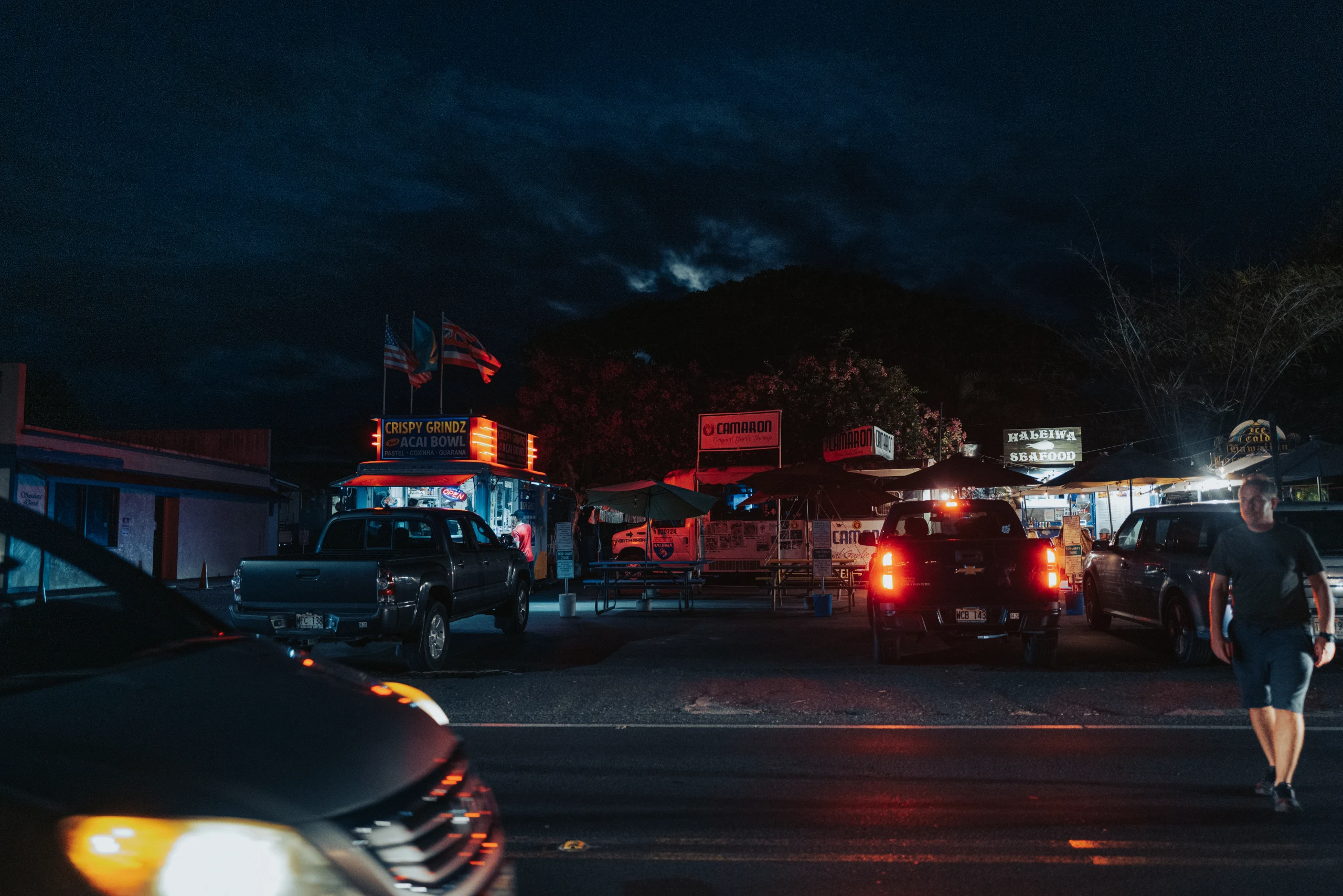 Cars and signs glow red at a roadside night market on O‘ahu.