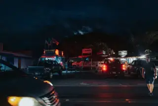 Cars and signs glow red at a roadside night market on O‘ahu.