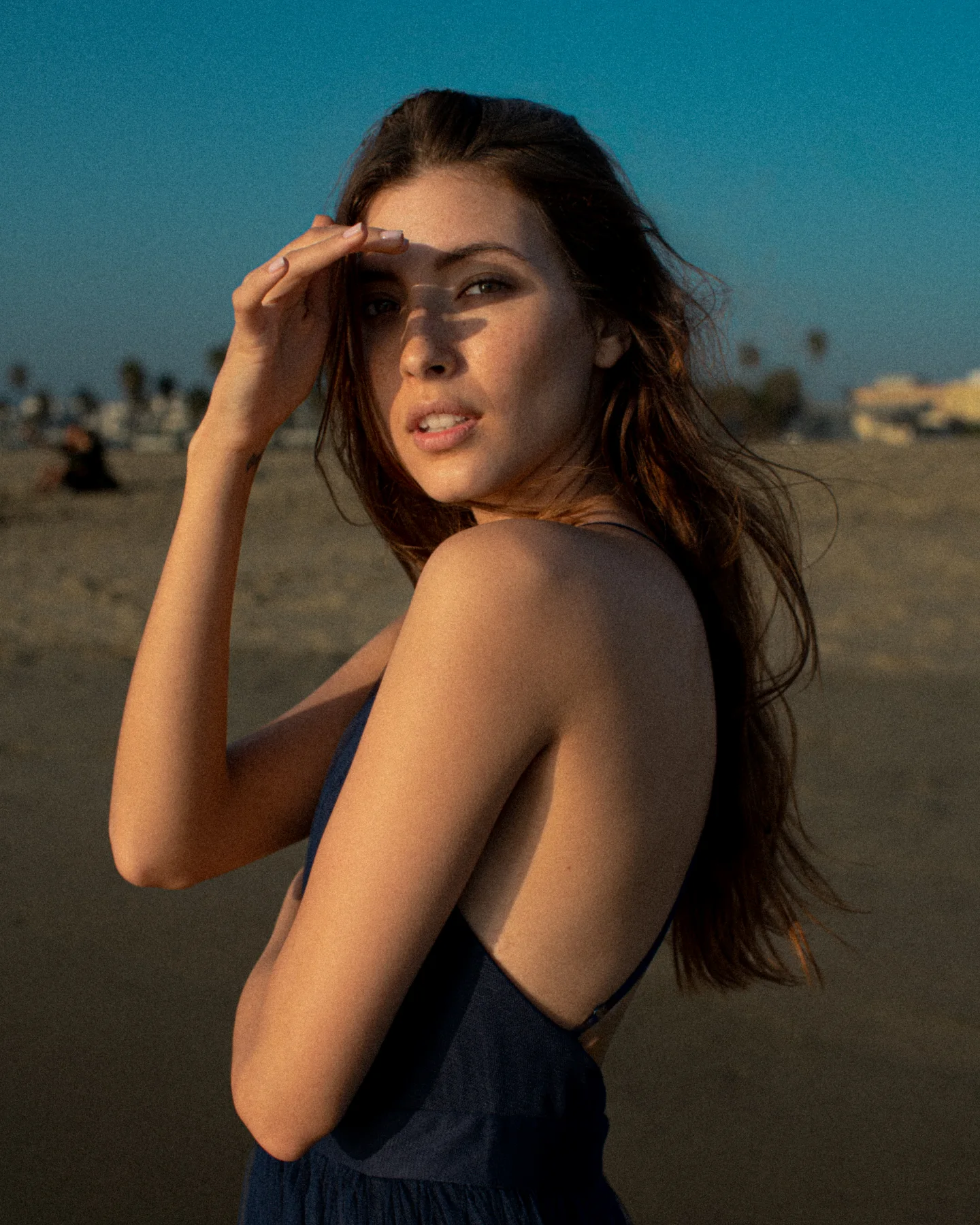 Woman shading her eyes in low coastal sunlight.
