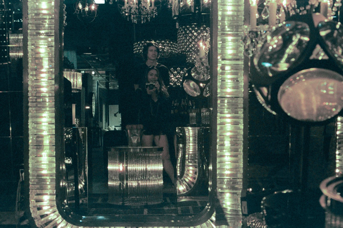 A woman is reflected among polished pipes and circular mirrors.