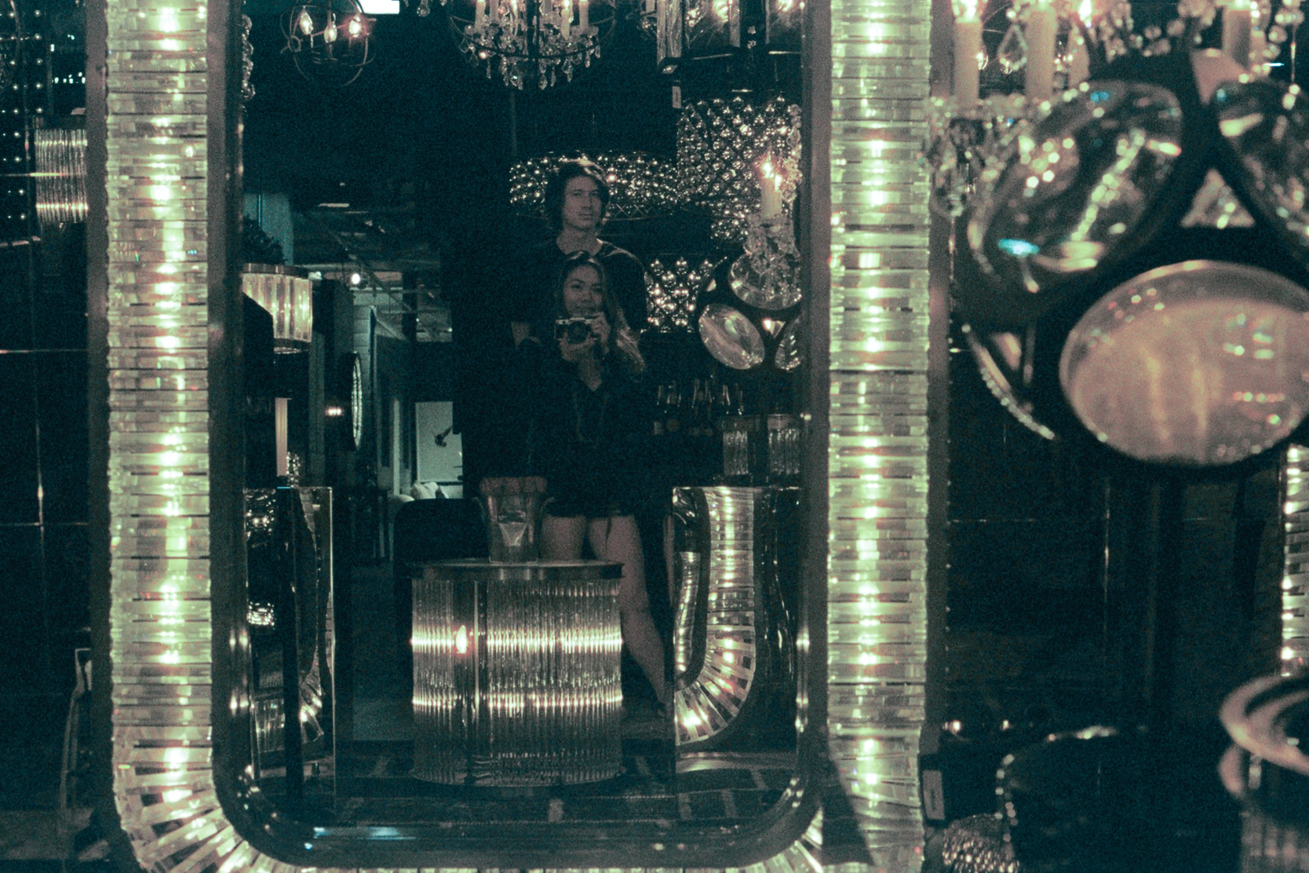 A woman is reflected among polished pipes and circular mirrors.